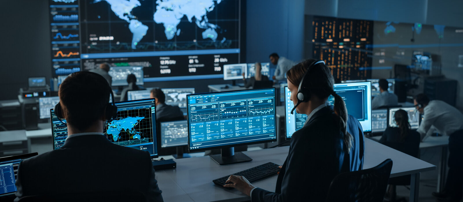 Female Specialist Works on a Computer with Live Ananlysis Feed from a Global Map on a Big Digital Screen. Employees Sit in Front of Displays with Financial Stock Market Trading Info and Big Data.